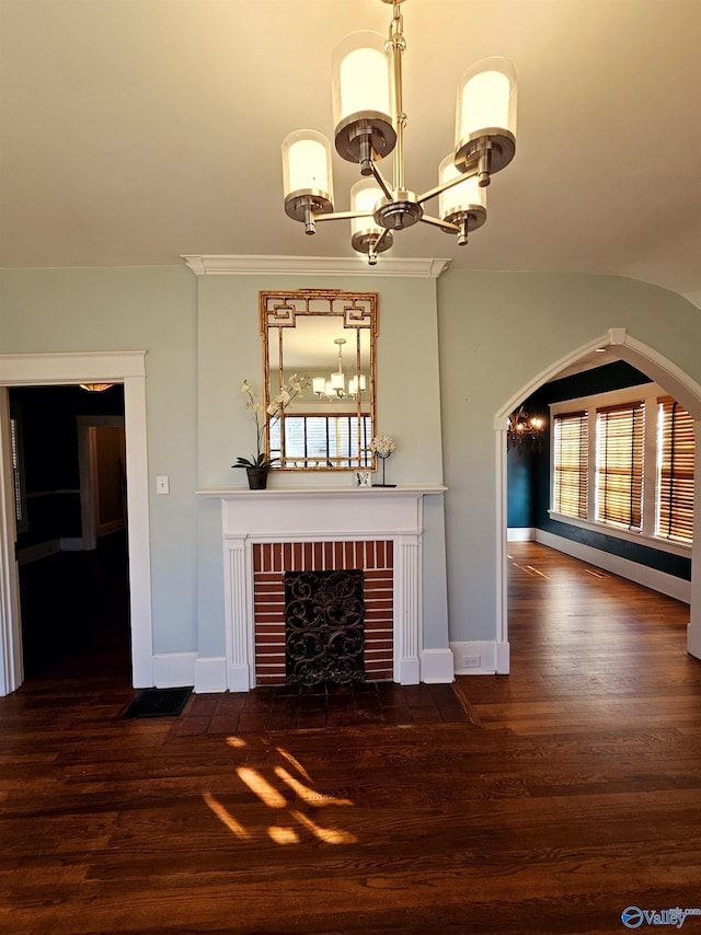 unfurnished living room featuring dark wood-type flooring, an inviting chandelier, a wealth of natural light, and a brick fireplace