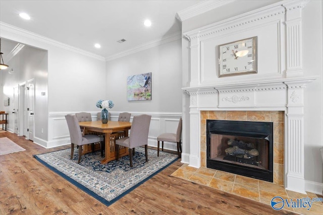 dining area with hardwood / wood-style flooring, a tiled fireplace, and crown molding