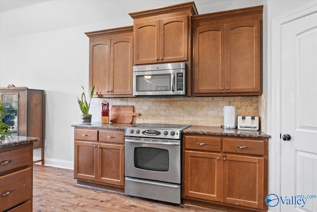 kitchen featuring appliances with stainless steel finishes, light hardwood / wood-style floors, dark stone counters, and decorative backsplash