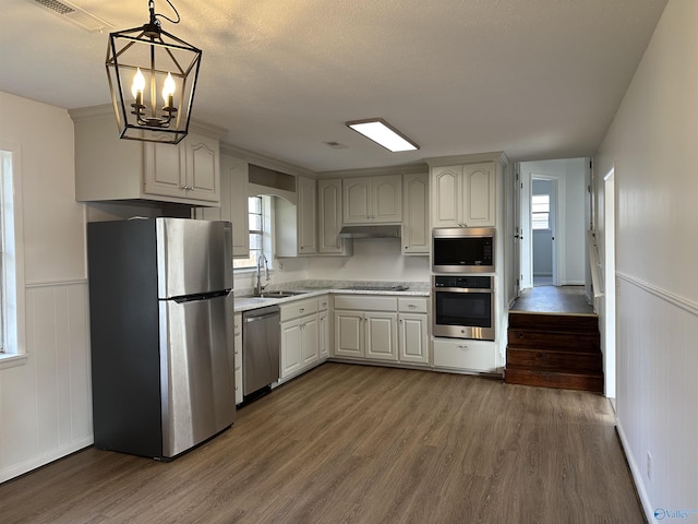 kitchen with sink, dark wood-type flooring, appliances with stainless steel finishes, white cabinets, and decorative light fixtures