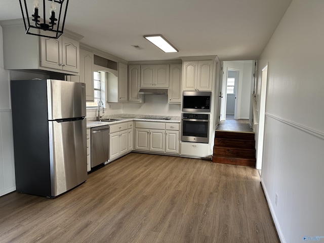 kitchen with hanging light fixtures, appliances with stainless steel finishes, sink, and light hardwood / wood-style floors