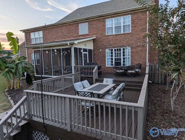 back house at dusk featuring a sunroom and a deck