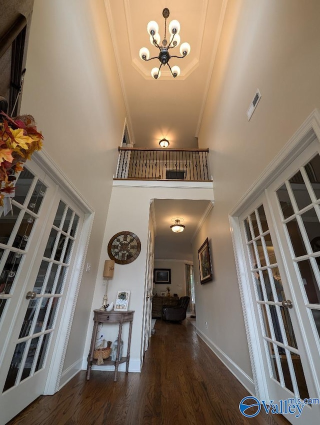 foyer with french doors, dark wood-type flooring, a notable chandelier, a towering ceiling, and ornamental molding