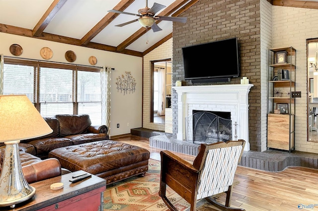 living room featuring beamed ceiling, a fireplace, wood finished floors, and ceiling fan