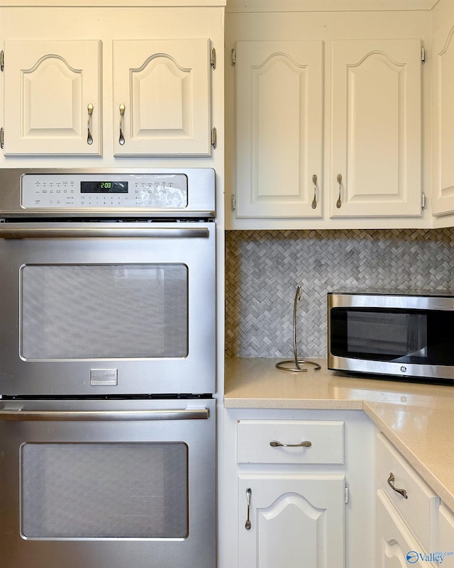 kitchen featuring stainless steel appliances, white cabinets, light countertops, and backsplash