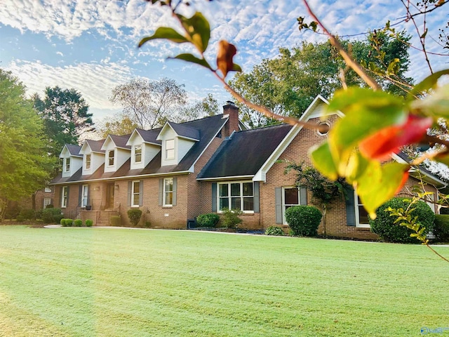 cape cod house featuring a front yard, brick siding, and a chimney