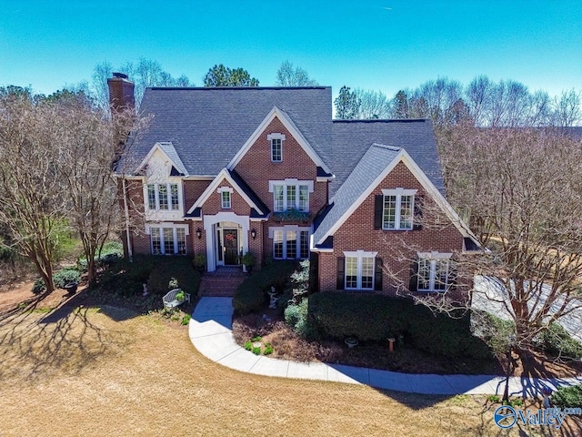 view of front of house with brick siding, a chimney, a front lawn, and roof with shingles