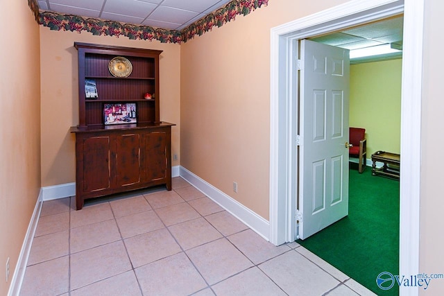corridor with light tile patterned flooring, baseboards, and a drop ceiling