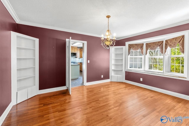 interior space featuring a notable chandelier, ornamental molding, hardwood / wood-style flooring, built in features, and baseboards