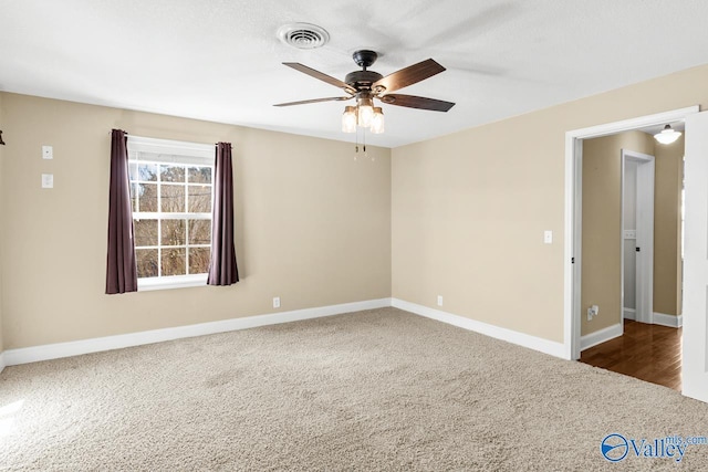 carpeted spare room with visible vents, baseboards, and a ceiling fan