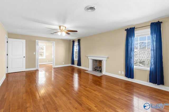 unfurnished living room with visible vents, plenty of natural light, a ceiling fan, and hardwood / wood-style flooring