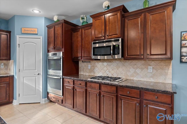 kitchen featuring backsplash, appliances with stainless steel finishes, light tile patterned floors, and dark stone countertops