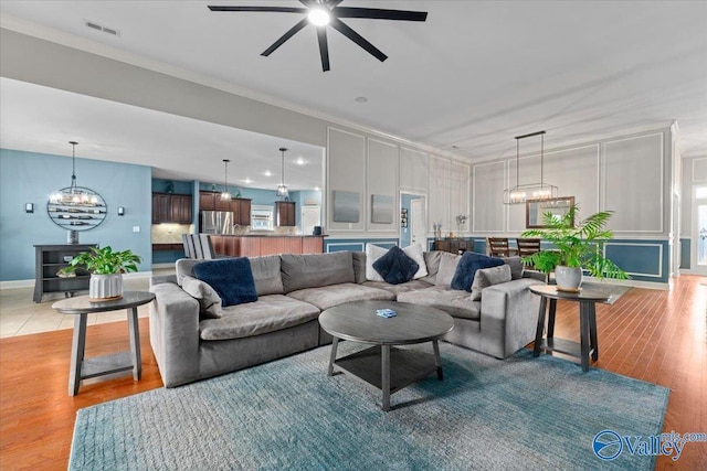 living room with ceiling fan with notable chandelier, ornamental molding, and light wood-type flooring