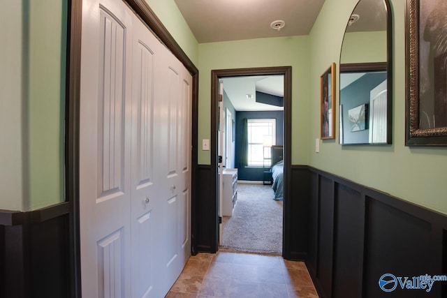 hall with wainscoting, light carpet, and light tile patterned floors