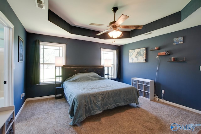 bedroom with multiple windows, a raised ceiling, baseboards, carpet flooring, and visible vents