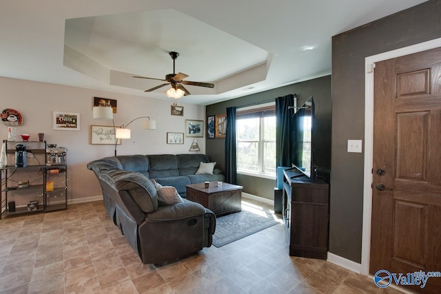 living room with a raised ceiling, a ceiling fan, and baseboards