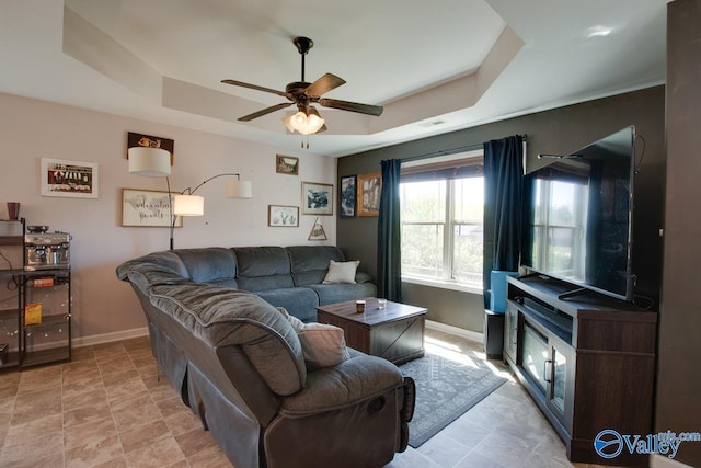 living area featuring ceiling fan, baseboards, visible vents, and a raised ceiling