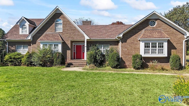 view of front facade with roof with shingles, a chimney, a front lawn, and brick siding
