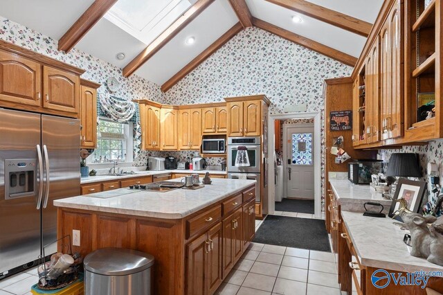 kitchen featuring a sink, light tile patterned floors, lofted ceiling with skylight, stainless steel appliances, and wallpapered walls