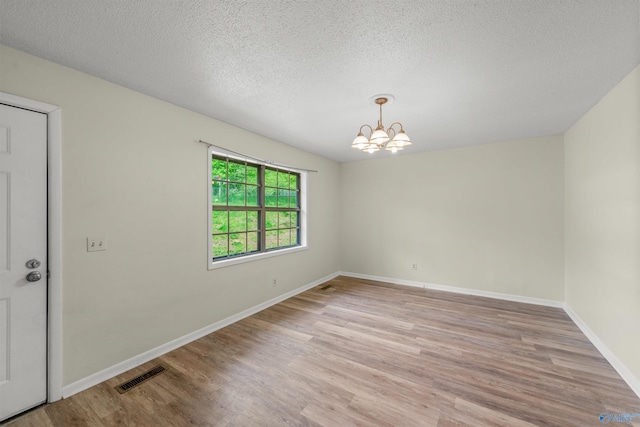 spare room with a textured ceiling, an inviting chandelier, and light hardwood / wood-style flooring