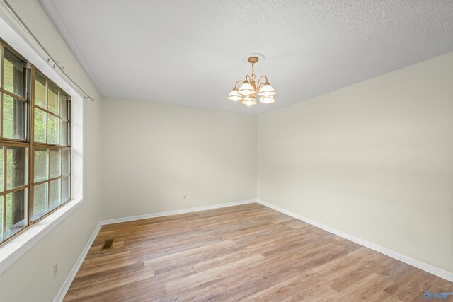 spare room featuring an inviting chandelier, hardwood / wood-style flooring, and a healthy amount of sunlight