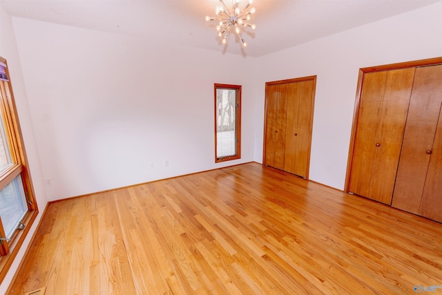 unfurnished bedroom with an inviting chandelier, light wood-style flooring, and two closets