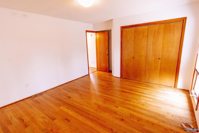 unfurnished bedroom with light wood-type flooring, a closet, visible vents, and a textured ceiling