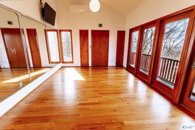 entrance foyer with an AC wall unit, high vaulted ceiling, and light wood-style flooring