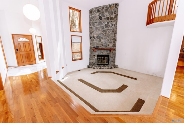 unfurnished living room featuring a towering ceiling, hardwood / wood-style flooring, visible vents, and a stone fireplace