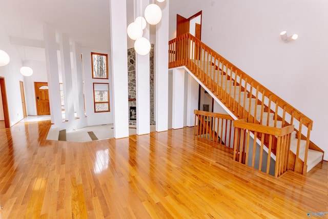 stairs featuring a stone fireplace, a towering ceiling, and hardwood / wood-style flooring