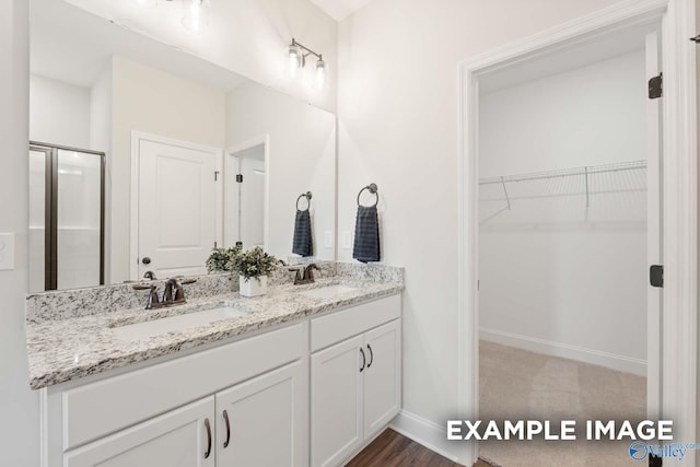 bathroom featuring double vanity, a sink, a walk in closet, and a stall shower