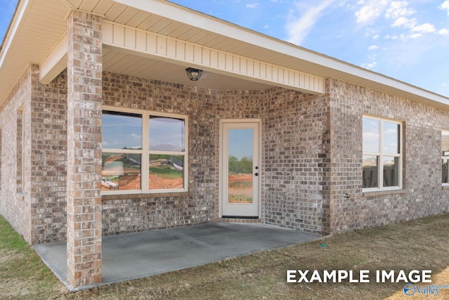 view of exterior entry featuring brick siding and a patio