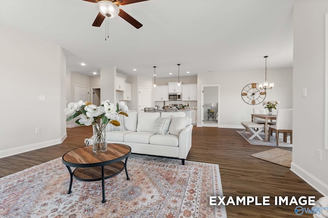 living area featuring ceiling fan with notable chandelier, baseboards, and dark wood-style flooring