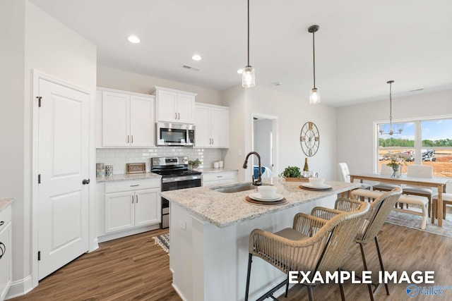 kitchen with stainless steel appliances, dark wood-style floors, a sink, tasteful backsplash, and a breakfast bar