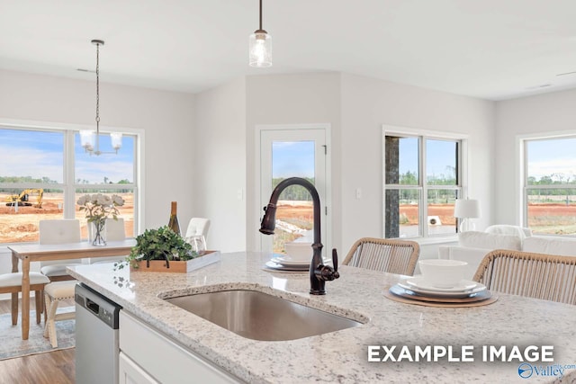 kitchen with light stone counters, wood finished floors, a sink, dishwasher, and pendant lighting
