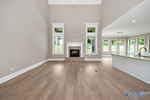 unfurnished living room with a high ceiling, plenty of natural light, a fireplace, and light hardwood / wood-style flooring