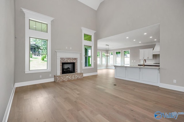 unfurnished living room with a brick fireplace, a towering ceiling, sink, and light wood-type flooring