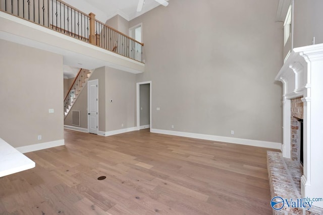 unfurnished living room with a brick fireplace, a towering ceiling, and light wood-type flooring