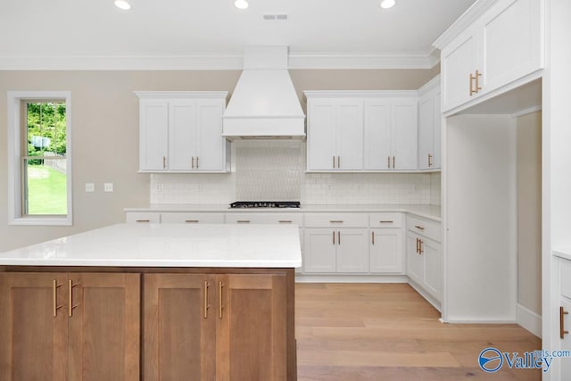 kitchen with white cabinetry, gas stovetop, custom exhaust hood, and a kitchen island