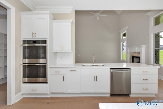 kitchen with appliances with stainless steel finishes, sink, white cabinets, crown molding, and light hardwood / wood-style flooring