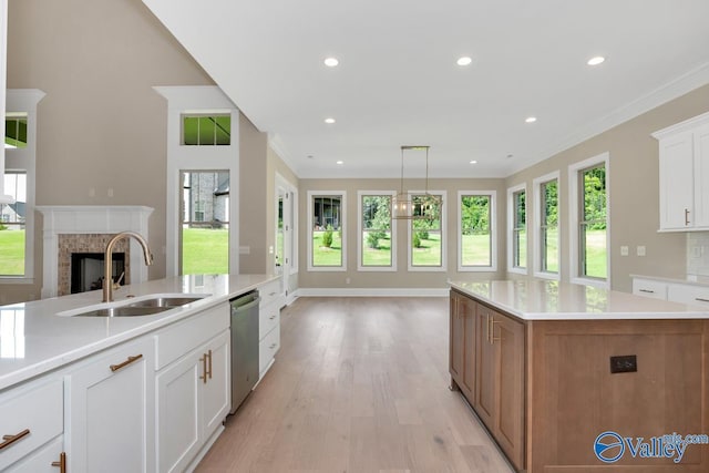 kitchen with sink, a brick fireplace, stainless steel dishwasher, an island with sink, and white cabinets