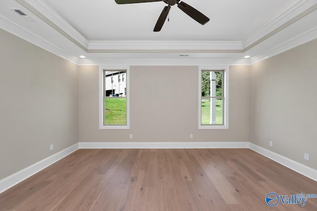 empty room with ornamental molding, a tray ceiling, and light wood-type flooring