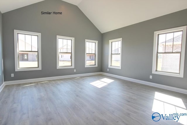 spare room featuring high vaulted ceiling, light wood finished floors, and baseboards