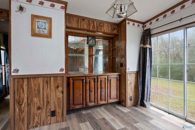 unfurnished dining area with hardwood / wood-style floors, wood walls, a textured ceiling, and crown molding