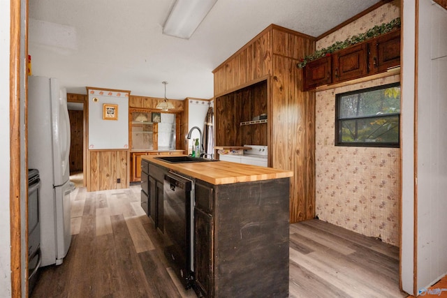 kitchen featuring butcher block counters, wood walls, sink, hardwood / wood-style floors, and black dishwasher