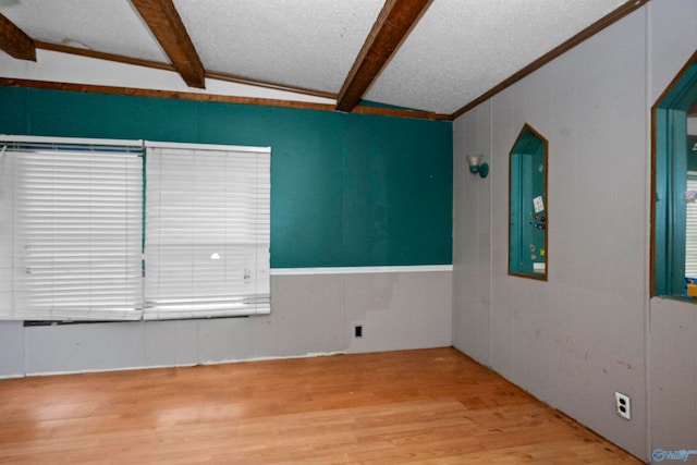 spare room featuring lofted ceiling with beams, a textured ceiling, hardwood / wood-style flooring, and crown molding