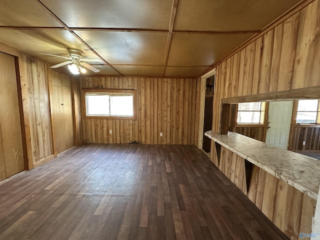 unfurnished room with ceiling fan, wood walls, and dark hardwood / wood-style flooring