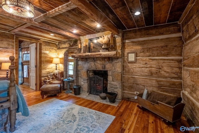 living room featuring beam ceiling, wooden ceiling, hardwood / wood-style floors, and a stone fireplace