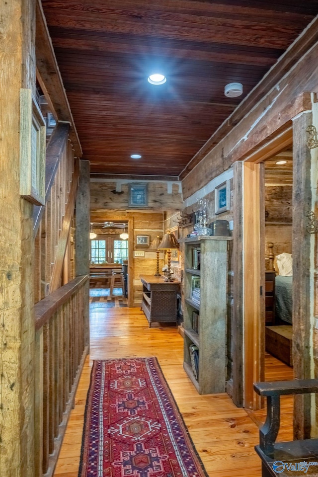 hallway featuring light hardwood / wood-style flooring, wood walls, and wooden ceiling