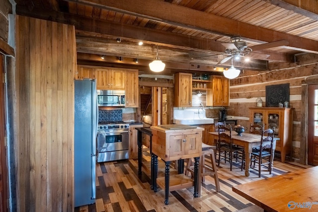 kitchen featuring appliances with stainless steel finishes, decorative backsplash, wood walls, ceiling fan, and hardwood / wood-style flooring